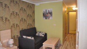 A small living area with a sofa, a side table, a lamp, a wall with a cityscape painting, and a patterned wallpaper.
