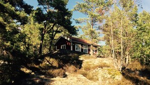 A cabin surrounded by trees, with a rocky landscape and a clear sky. - Lövhagens Café & Vandrarhem (Nynashamn)