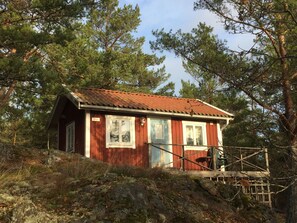 Een kleine hut met een rode gevel, een houten terras en uitzicht op de omliggende bomen.