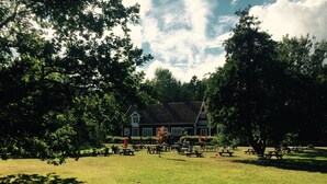 A large, open grassy area with picnic tables and a building in the background. - Lövhagens Café & Vandrarhem (Nynashamn)