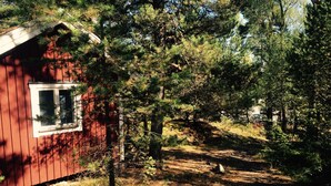 A red cabin with a window, surrounded by dense forest and a dirt path. - Lövhagens Café & Vandrarhem (Nynashamn)