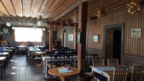 A rustic dining area with wooden tables and chairs, hanging flower arrangements, and a view of the outdoors through large windows. - Lövhagens Café & Vandrarhem (Nynashamn)