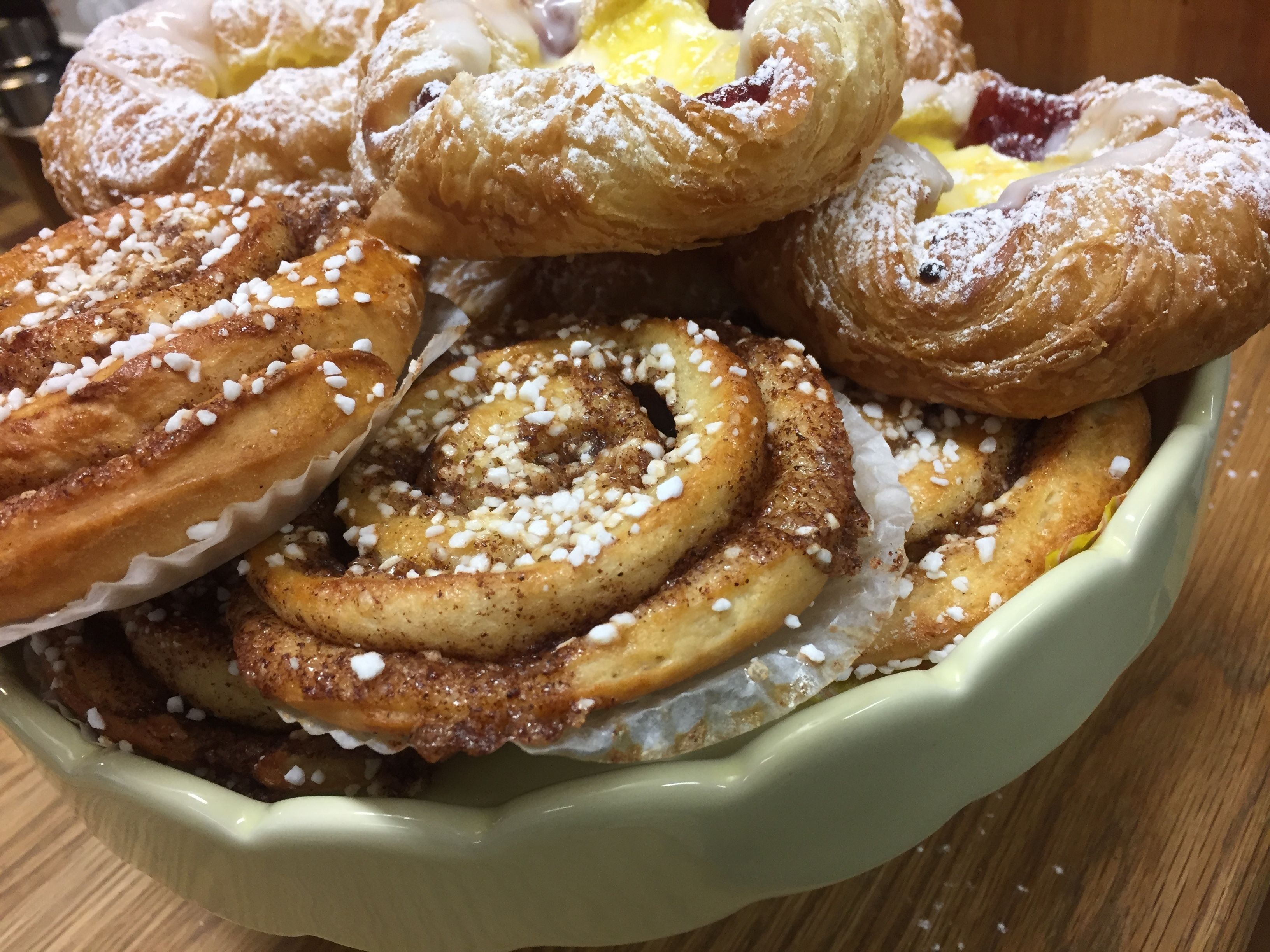 A bowl of pastries, including cinnamon rolls and pastries with powdered sugar and fruit.