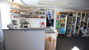 A reception area with a counter, shelves with various items, a fire extinguisher, and a vending machine. - Old Camp (Kangerlussuaq)