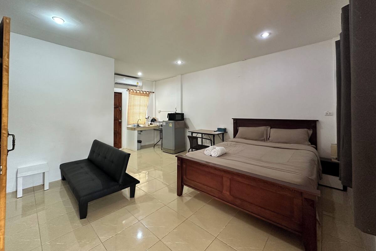 A bedroom with a bed, a desk, a chair, and a kitchenette.