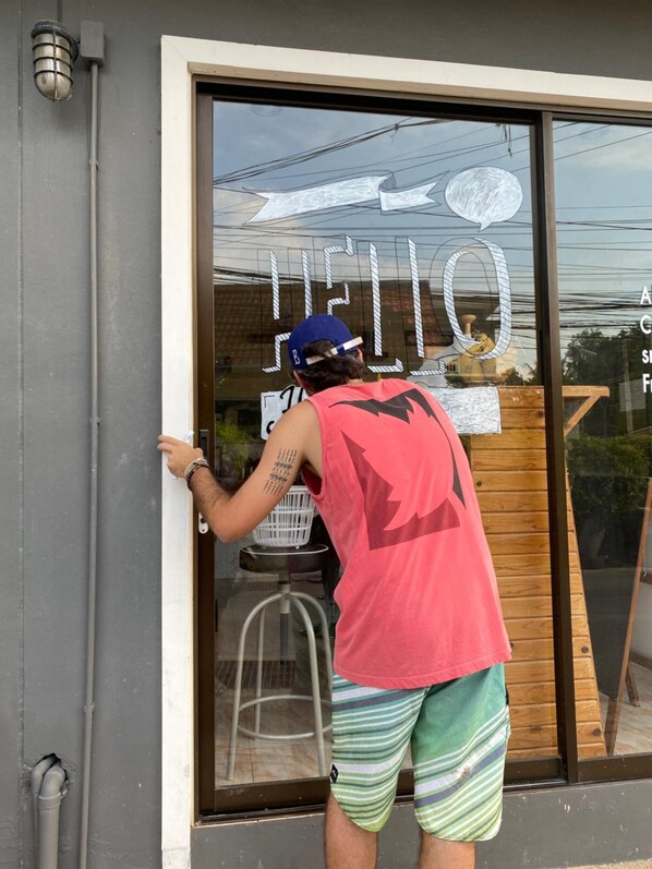 A person painting a window with the word "HELLO" on it. - Bangtao Corner (Choeng Thale)