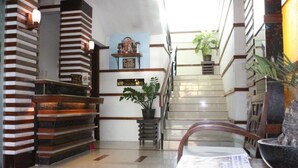 Ein Hotel-Empfangsbereich mit Empfangstresen, einer Treppe und einer Zimmerpflanze.
