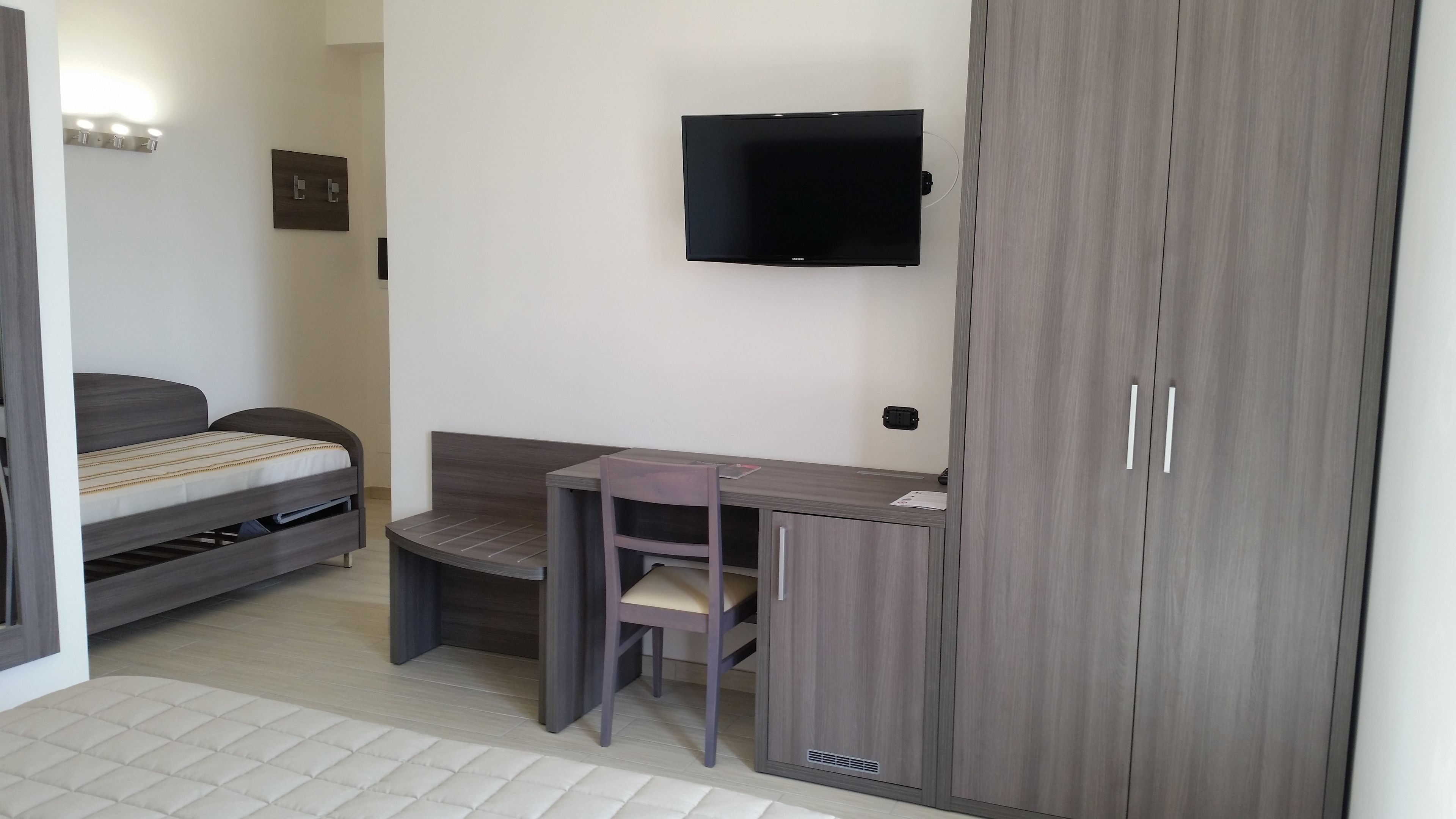 Ein kleines Schlafzimmer mit Bett, Schreibtisch und einem an der Wand befestigten Fernseher.