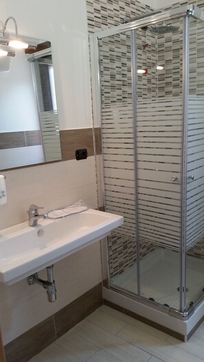 A modern bathroom with a glass shower enclosure, a white sink, and a tiled backsplash. - Belsito (Serrone)