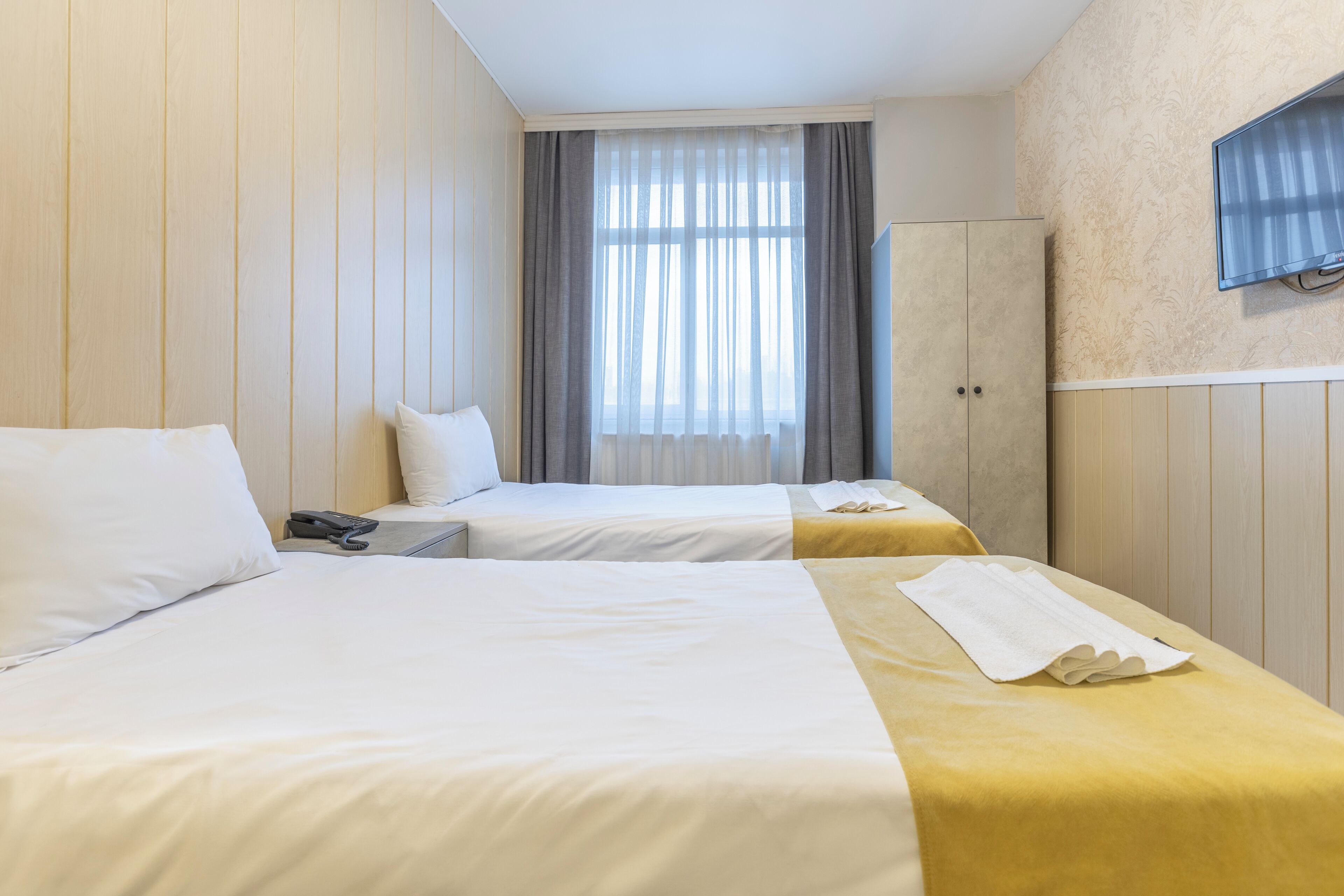 A hotel room with two beds, a TV mounted on the wall, and a window with curtains.