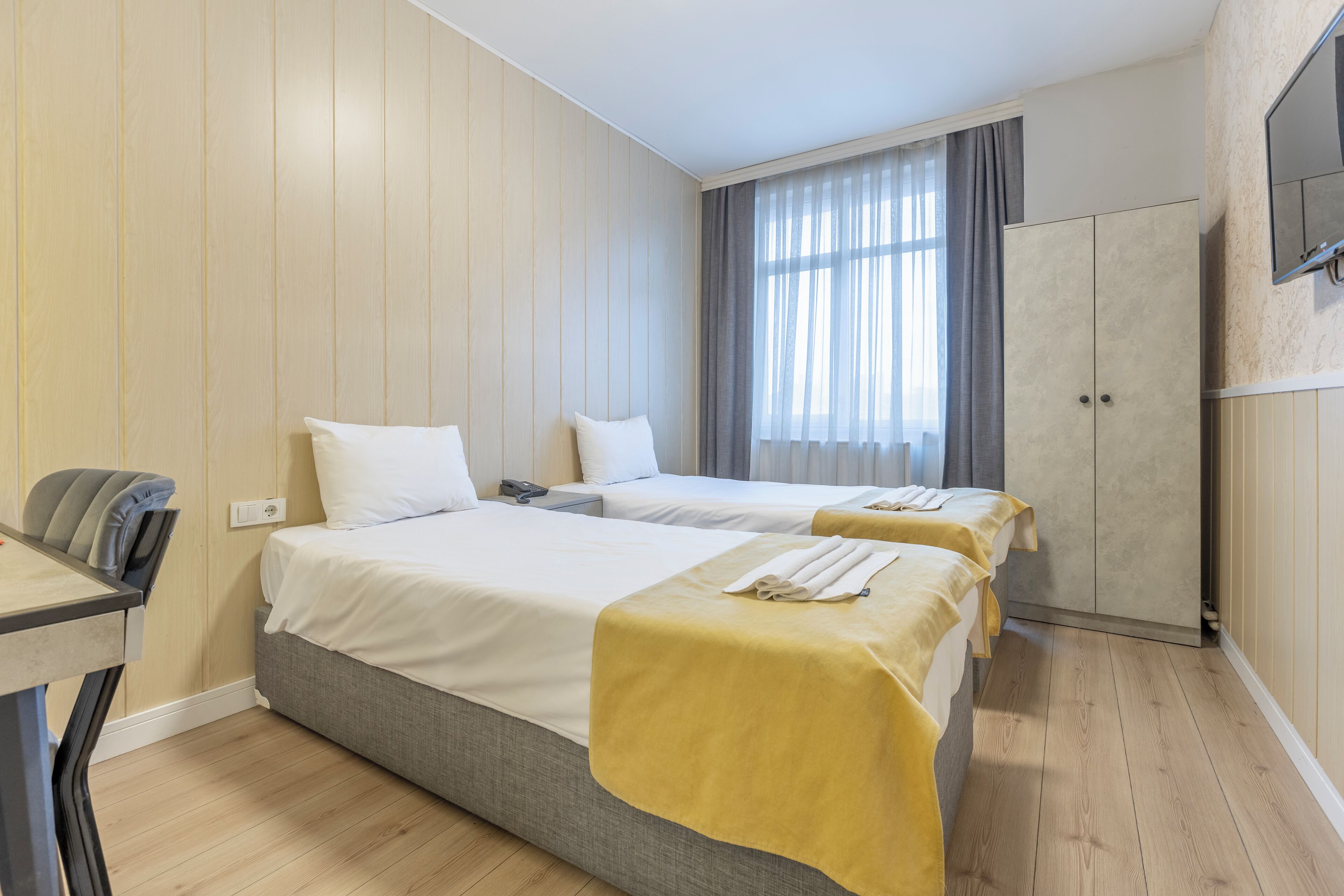 A hotel room with two beds, a desk, a wardrobe, and a TV on the wall.