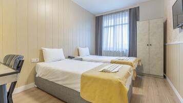 A hotel room with two beds, a desk, a wardrobe, and a TV on the wall.