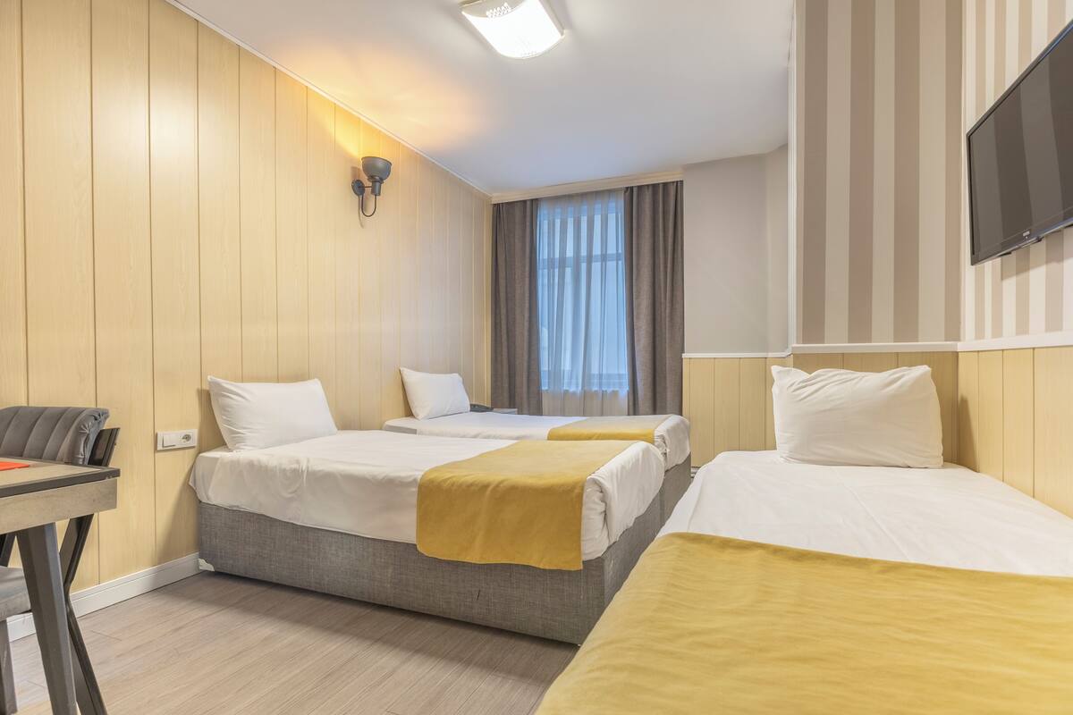 A hotel room with two beds, a desk, a TV, and a window with curtains.