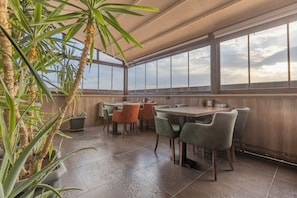 Un restaurante con terraza, mesas, sillas y plantas en macetas.