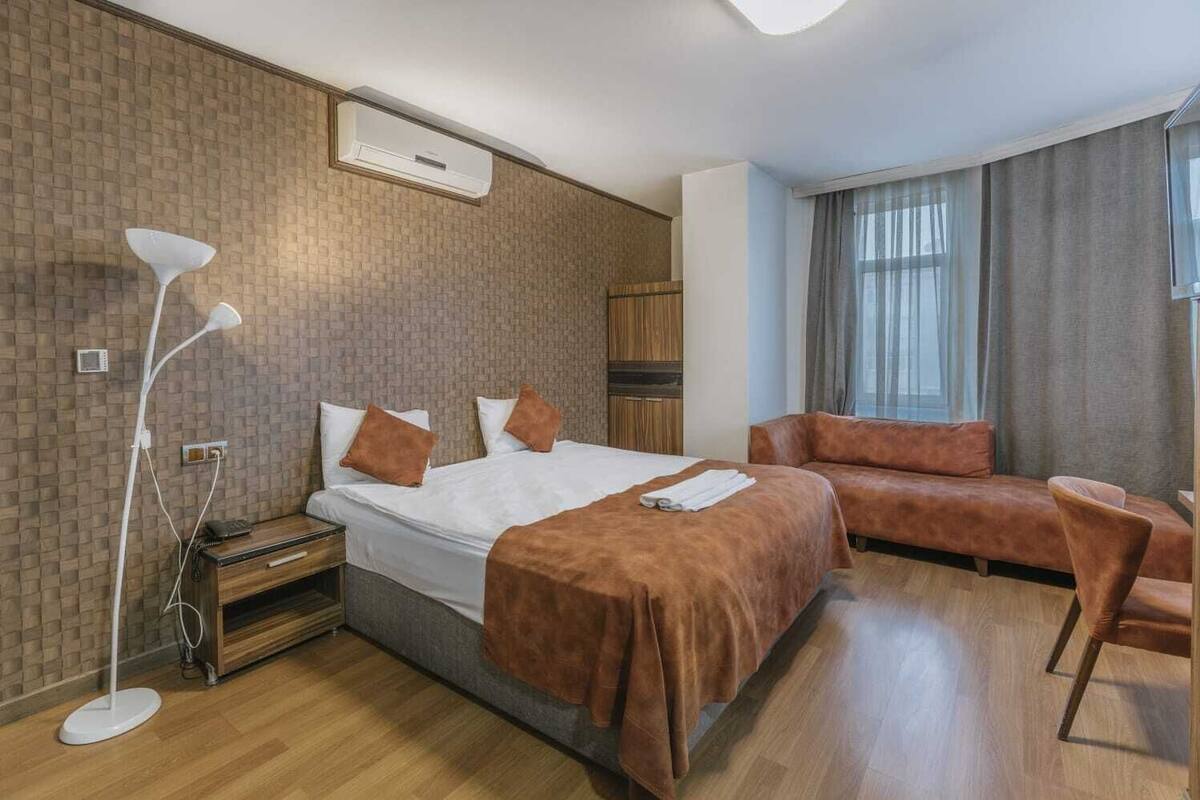 A hotel room with a bed, a sofa, a desk, and a lamp.