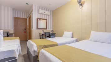 Quarto de hotel com três camas de solteiro, uma mesa de escritório com cadeira, um espelho e ar condicionado.