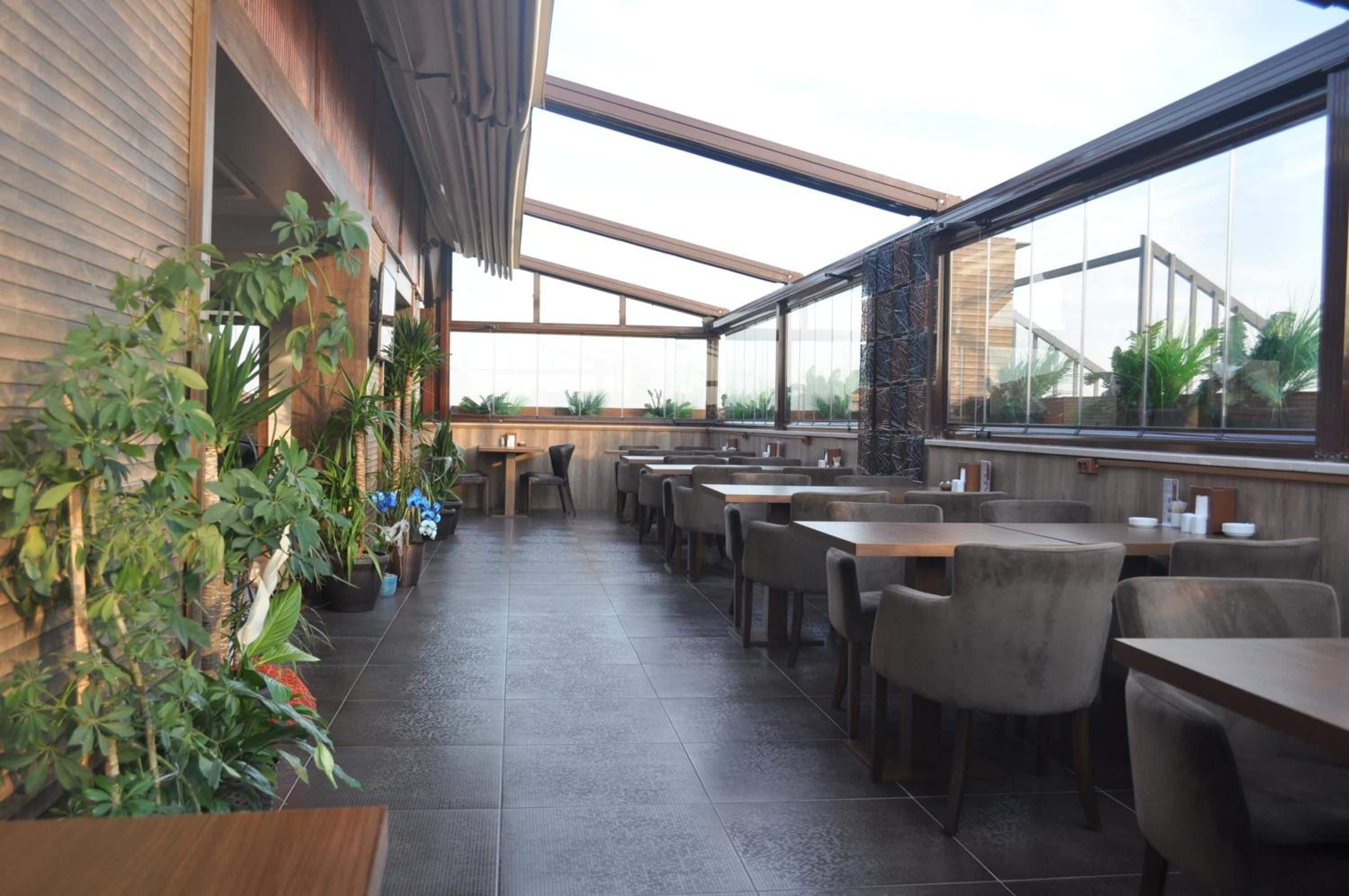 A restaurant with a modern interior, featuring a long counter with multiple seating options and a variety of plants.
