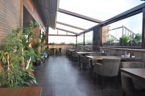 Un restaurante con un interior moderno, que cuenta con una larga barra y diversas opciones de asiento, además de una variedad de plantas.