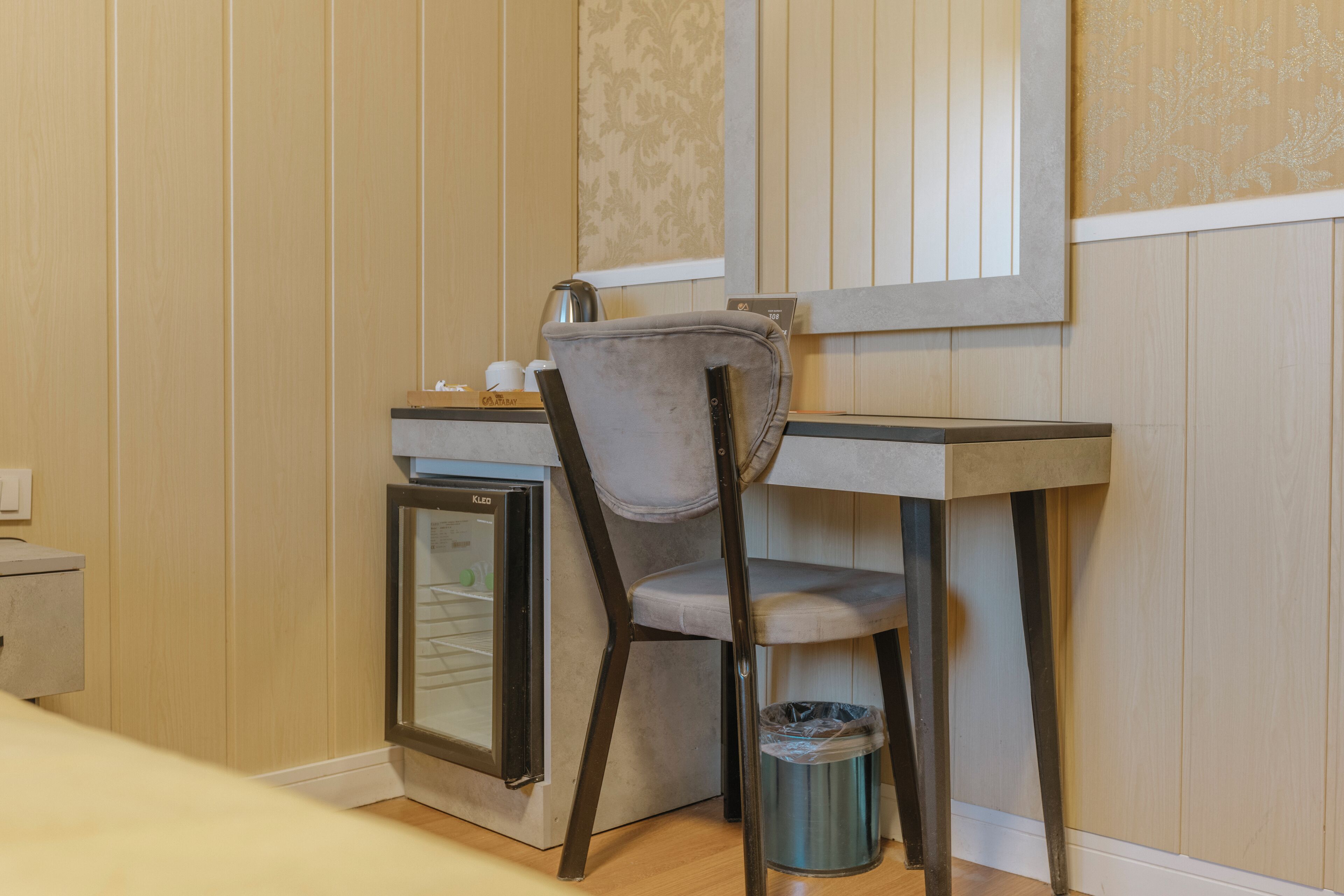 A compact kitchenette with a small refrigerator, a chair, and a trash bin.