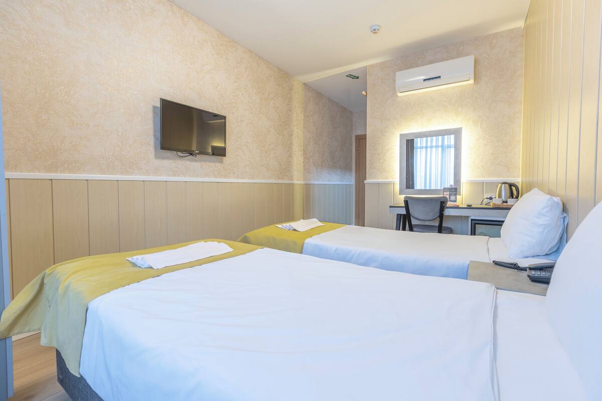 A hotel room with two beds, a desk, a chair, a television, and an air conditioning unit.
