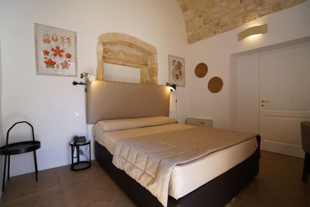 Une chambre à coucher comprenant un lit, une chaise, une petite table et un miroir fixé au mur.