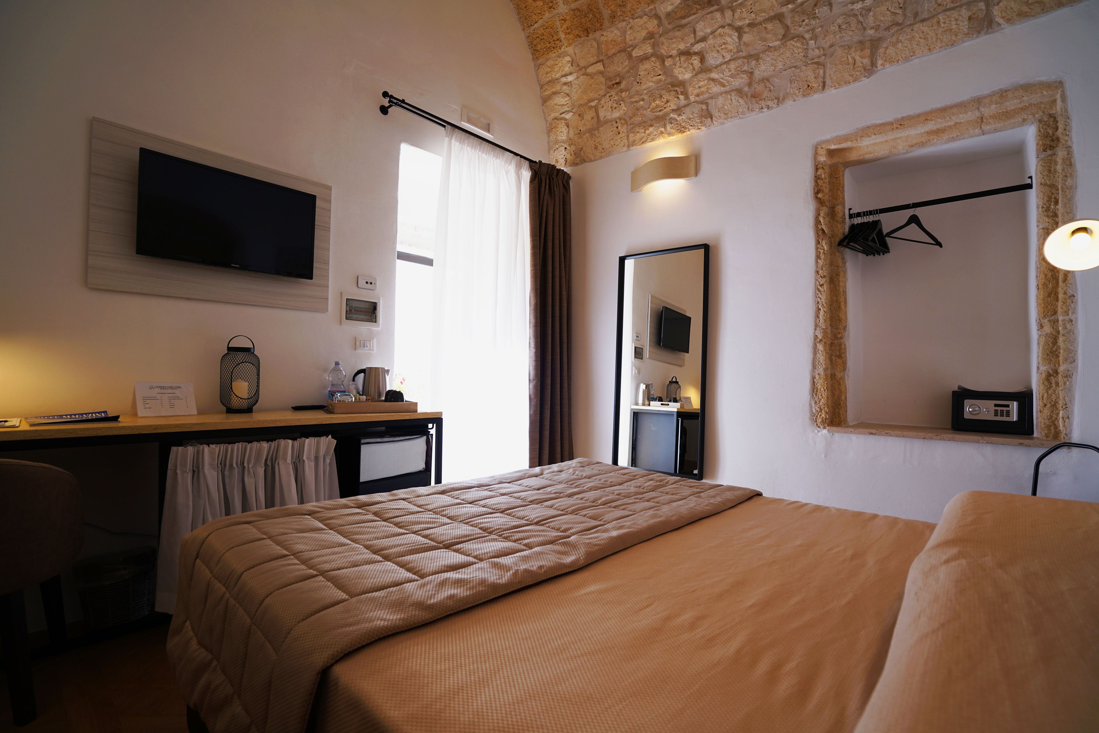 A hotel room with a bed, a desk, a television, a mirror, and a window with curtains.