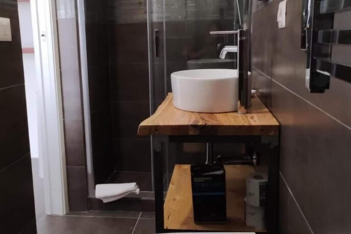 Une salle de bain avec une douche à parois de verre, un lavabo blanc posé sur un meuble-vasque en bois et un porte-serviettes fixé au mur.