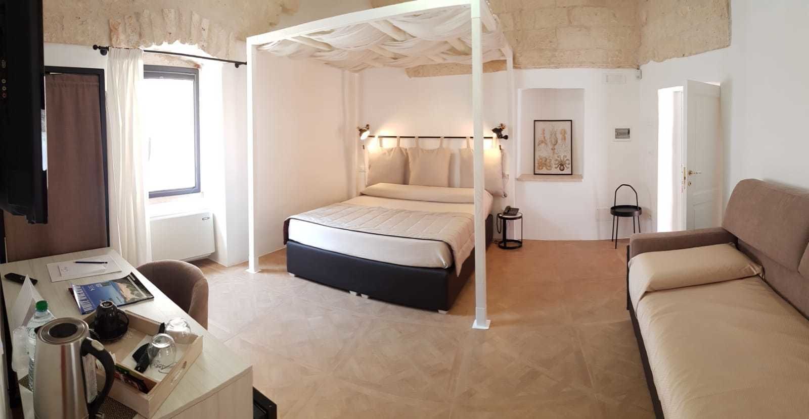 Ein Schlafzimmer mit Bett, Schreibtisch mit Stuhl, Sofa, Nachttisch und einer Wandlampe.