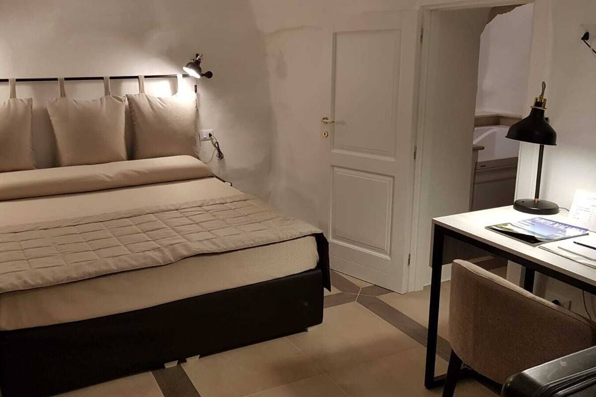 Une chambre bien rangée, avec un lit, une table de chevet, une lampe et un bureau avec une chaise.