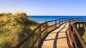 A wooden boardwalk leading to a beach with clear blue water and grassy dunes. - Dimora Sant'Anna (Carovigno)