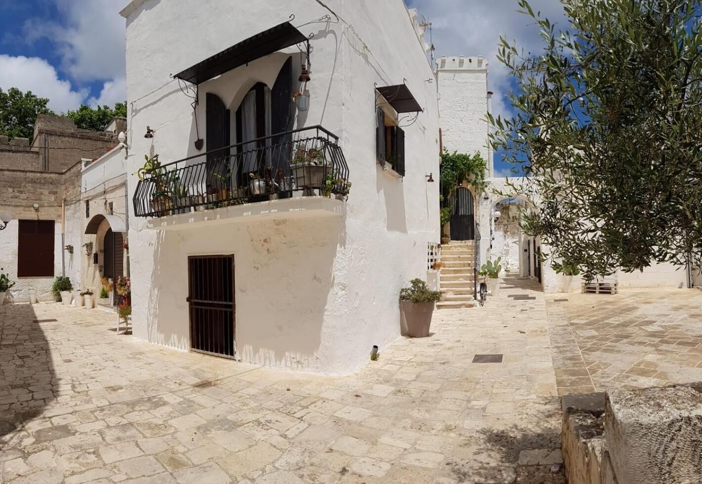 Un edificio blanco con un balcón, una puerta y una escalera que lleva a una torre.