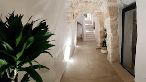 A narrow hallway with a stone archway leading to a staircase. There are potted plants along the walls and a door on the right. - Dimora Sant'Anna (Carovigno)