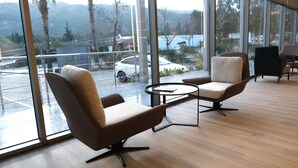 A modern room with two leather chairs, a small table, and large windows offering a view of a parking area and mountains. - Hotel Buyuk Saruhan (Manisa)