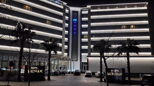 A modern hotel with horizontal lighting strips, a central entrance, and palm trees. - Hotel Buyuk Saruhan (Manisa)