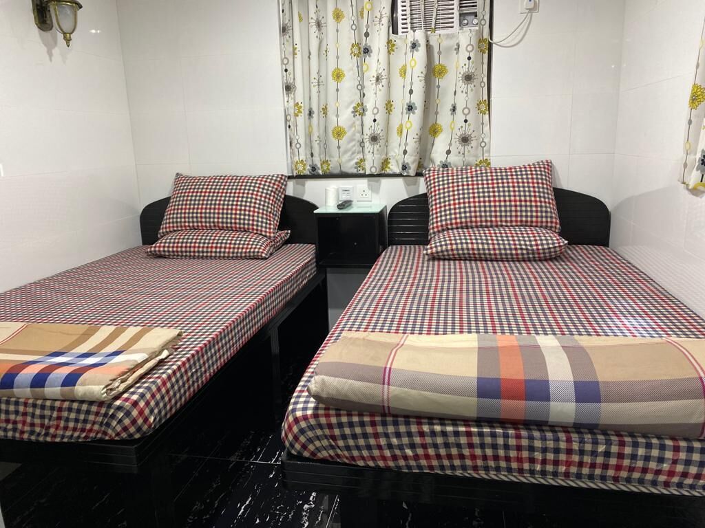 Habitación de hotel con dos camas individuales, una mesita, una silla y un ventanal con cortinas.