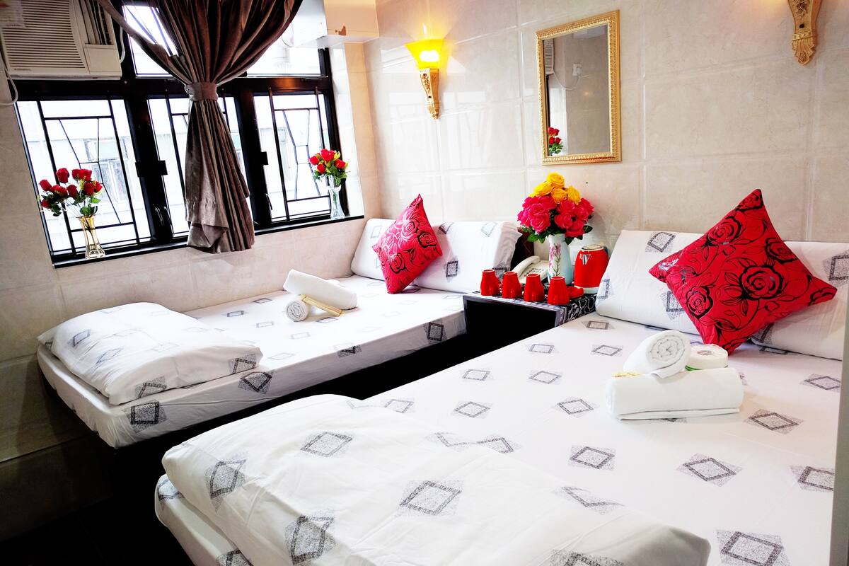 Une chambre d’hôtel avec deux lits simples, un canapé-lit, une petite table ornée d’un vase de fleurs et un miroir au mur.