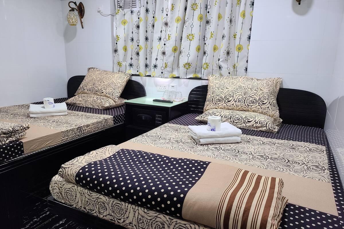 Une chambre d’hôtel avec deux lits, chacun agrémenté de draps et d’oreillers à motifs, une table de chevet avec une télécommande et un rideau orné de motifs floraux.