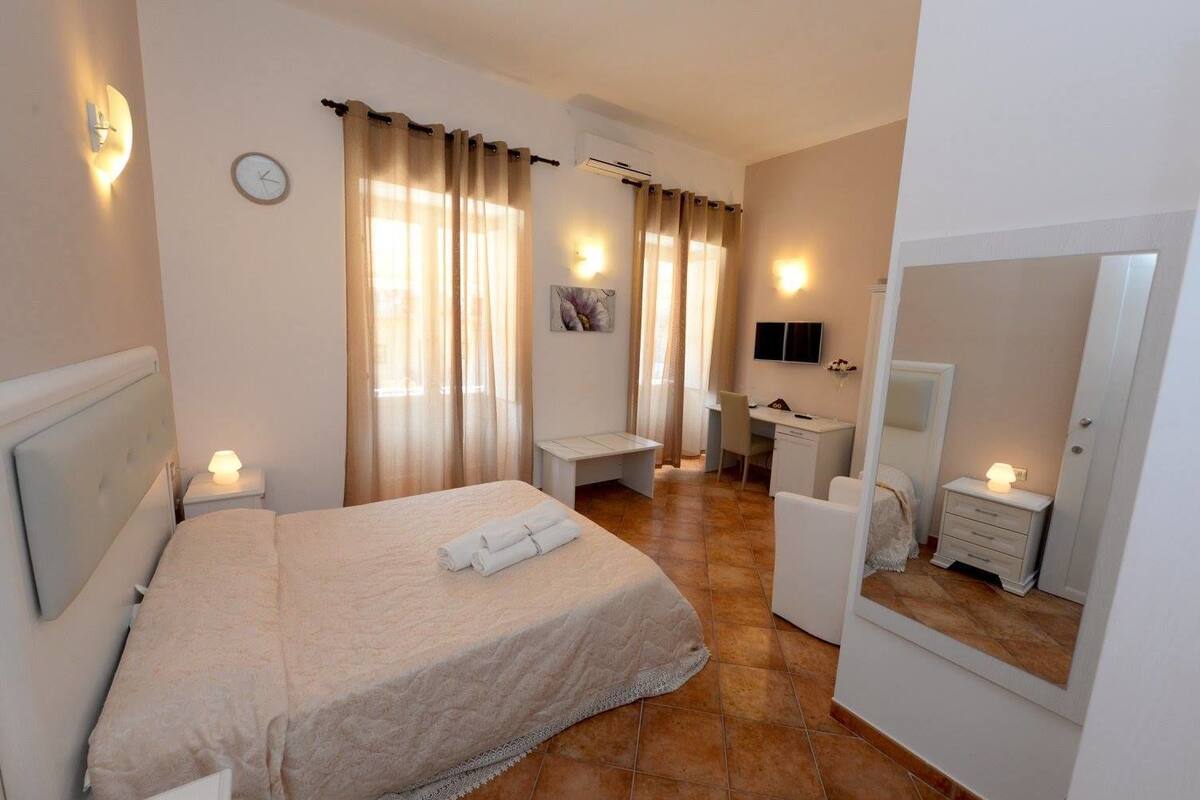 A hotel room with a bed, a desk, a chair, a TV, and a mirror.