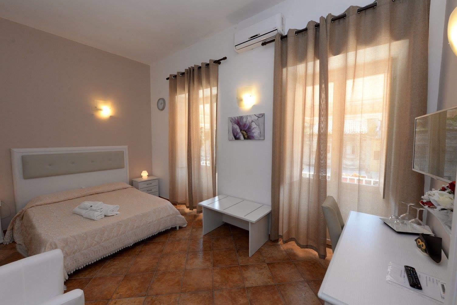 A hotel room with a bed, bedside table, desk, chair, and a TV.