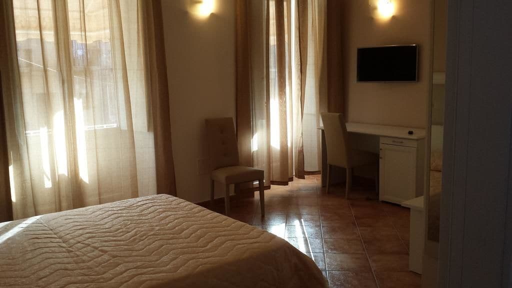 A hotel room with a bed, a desk, a chair, and a television on the wall.