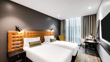Una habitación de hotel con dos camas, un escritorio, una silla y un ventanal con cortinas.