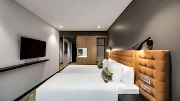 Une chambre d’hôtel moderne avec un grand lit, un téléviseur à écran plat fixé au mur et une table de chevet avec une lampe.