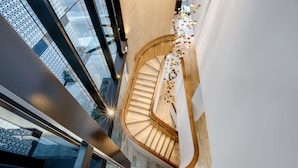 Un escalier en colimaçon moderne, avec une finition en bois et des rampes en verre, menant à un étage supérieur d’où l’on peut admirer la vue sur la ville.