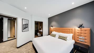 Une chambre d’hôtel moderne avec un grand lit, une tête de lit dotée de commandes intégrées, une table de chevet et une œuvre d’art encadrée au mur.