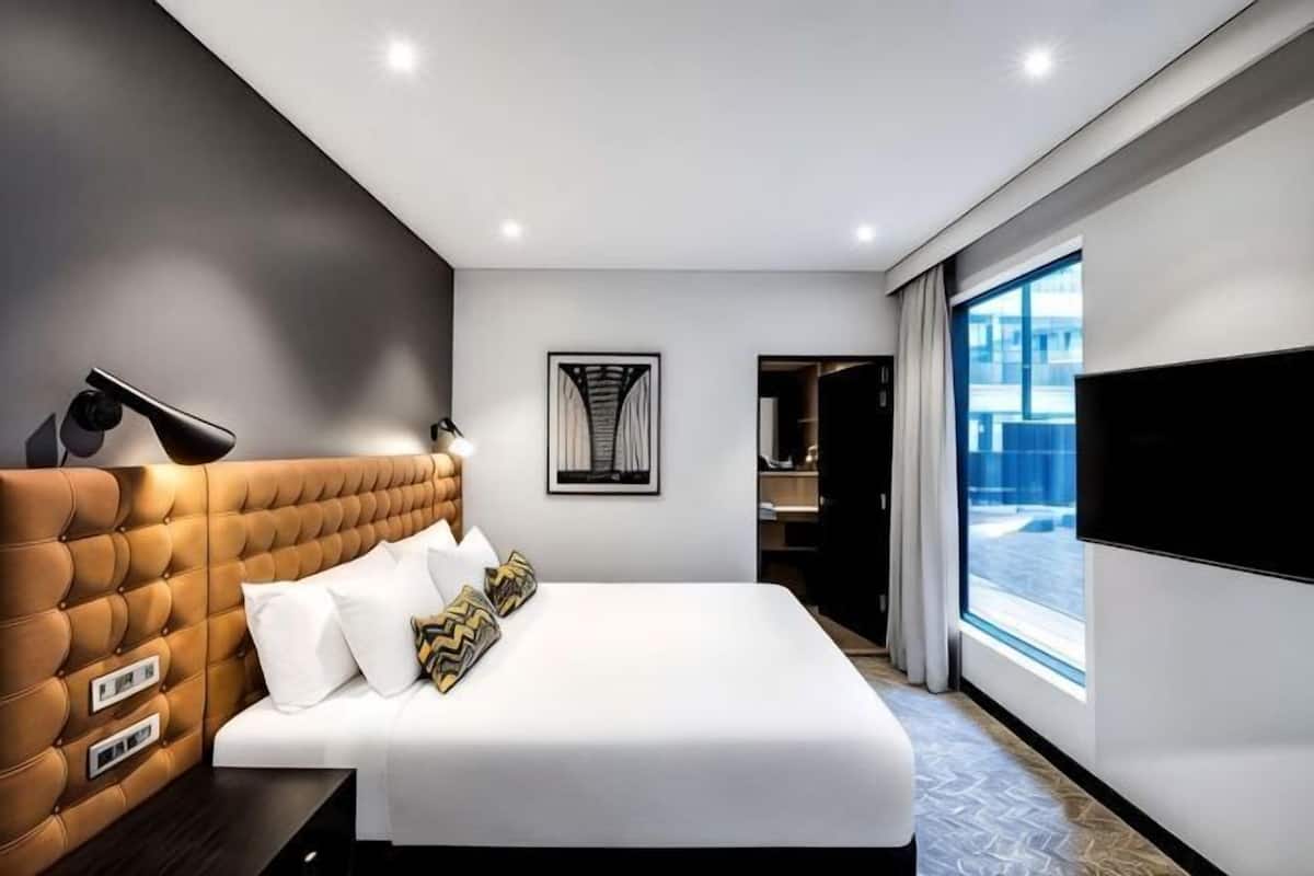 Ein modernes Hotelzimmer mit einer gepolsterten Kopfteil, einem großen Bett mit weißen Leinentüchern, einem Flachbildfernseher und einem großen Fenster mit Aussicht.