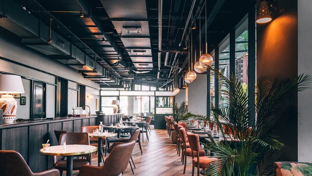 Un intérieur de restaurant moderne avec un plancher en bois, des fauteuils en cuir et des luminaires suspendus.