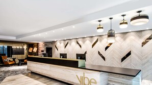 Un espace d’accueil doté d’un comptoir de réception en marbre, d’un éclairage moderne suspendu et d’un mur orné d’un motif en chevrons.