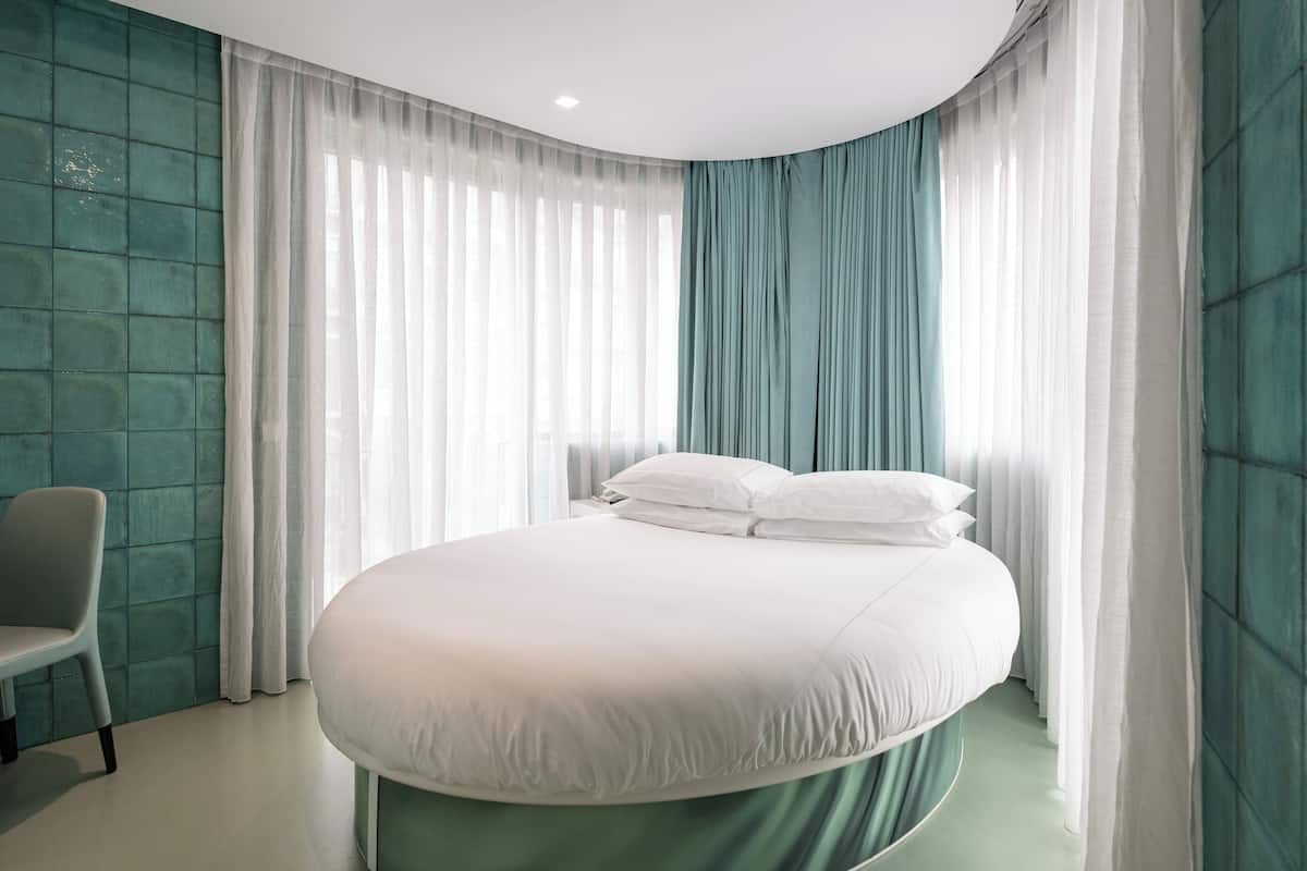 Un dormitorio moderno con una cama curvada, una silla y cortinas de gasa.