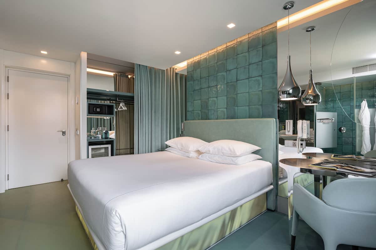 Una habitación de hotel moderna con una cama grande, un escritorio, un espejo y un armario.
