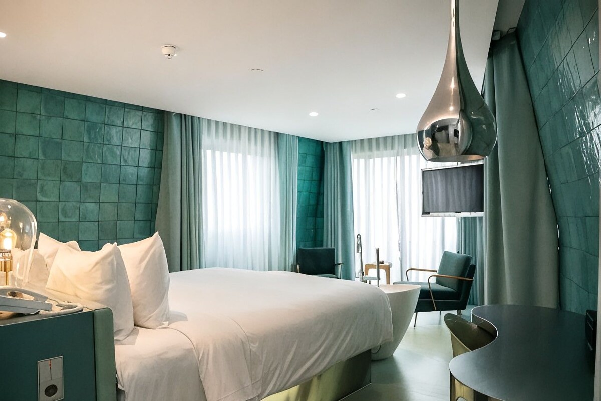 A modern hotel room with a large bed, a desk, and a chair.